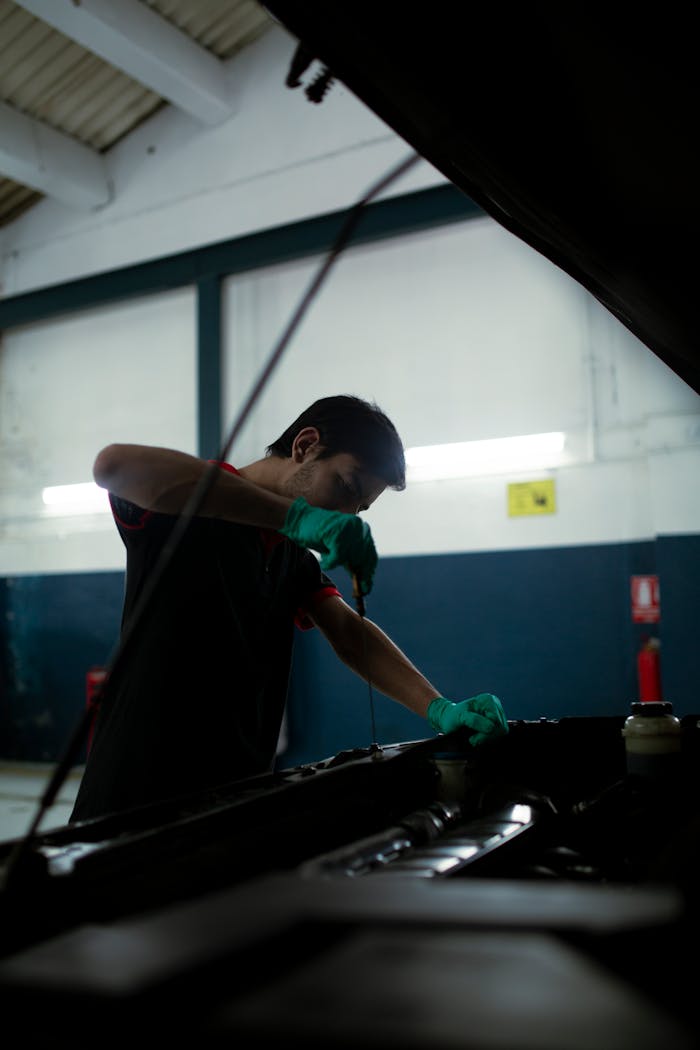 Mechanic checks engine oil in a car inside an auto garage, highlighting routine maintenance.