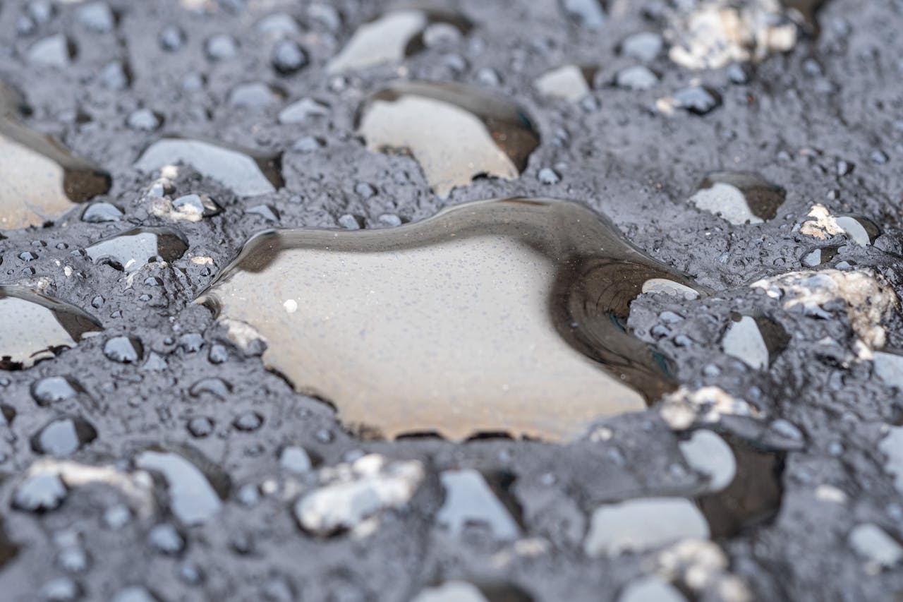Detailed view of wet asphalt surface showing reflections in water puddles.