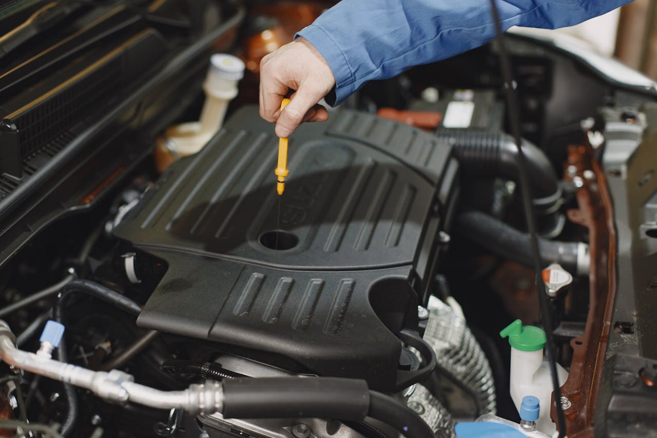 services-01 Close-up of a person checking engine oil using a dipstick in a car's engine bay.